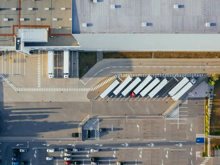 An aerial view of a distribution centre, with trailers backed into the loading docks and a row of others parked alongside.