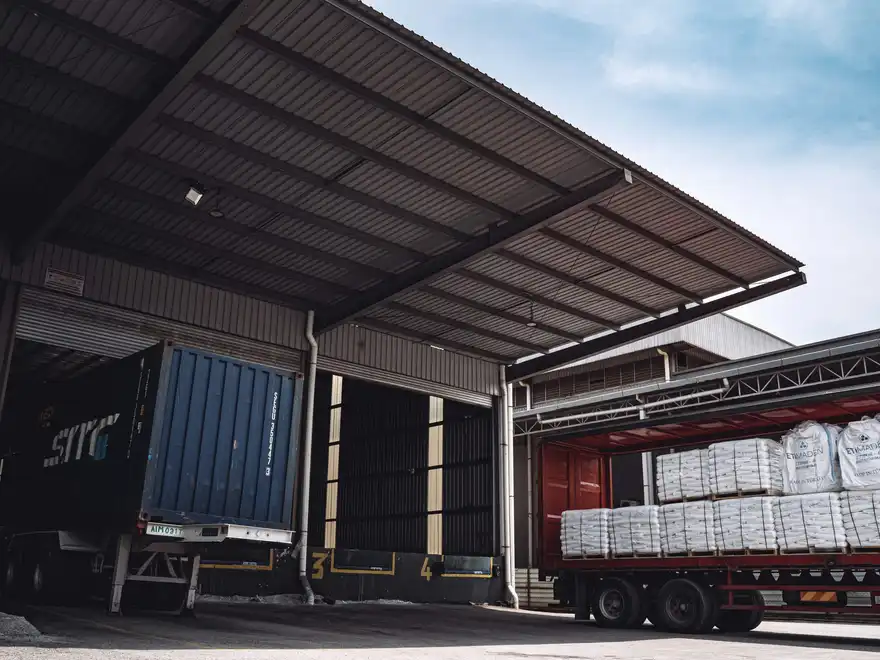 Container trucks and a loaded trailer backed into the dispatch bays of a warehouse.