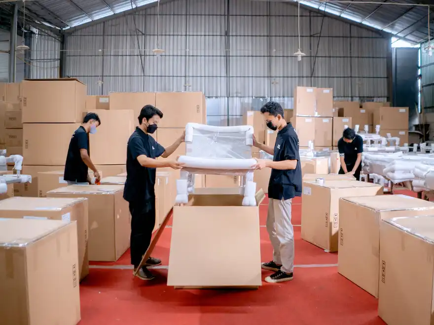 A team of warehouse workers in uniform packing and wrapping cartons on a depot floor.
