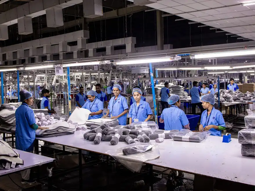 Factory workers in uniform folding and packing textiles along a production line.