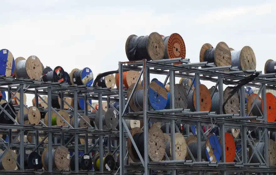 Steel racks stacked with large wooden reels of electrical cable in an open yard.